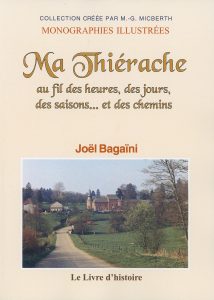 Couverture du livre intitulé « Ma Thiérache au fil des heures, des jours, des saisons… et des chemins » de Joël Bagaini, dans la collection « Monographies illustrées ». L’image de couverture montre une route de campagne qui mène vers un petit village thiérachien composé de maisons en briques et d’une église fortifiée entourée d’arbres et de prairies verdoyantes. En bas, figure la mention de l’éditeur « Le Livre d’histoire ».