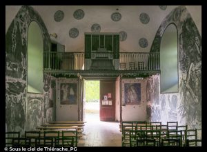 Intérieur de l’église Saint-Martin de Jeantes : vue vers la tribune et l’entrée, montrant les grandes fresques murales modernes en noir et blanc de Charles Eyck, représentant des scènes bibliques stylisées, avec les bancs en bois au premier plan et la lumière naturelle entrant par la porte ouverte.