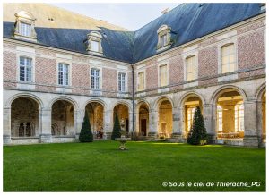 Cloître de l’abbaye de Saint-Michel en Thiérache, avec ses galeries voûtées en pierre, ses arcades, la façade en brique et pierre et le jardin central orné d’une fontaine.