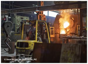 Intérieur de l’atelier de fusion des Fonderies de Sougland, où un chariot élévateur circule près d’un four ouvert laissant apparaître le métal en fusion incandescent dans la fonderie de Saint-Michel en Thiérache