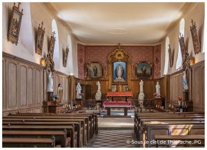 Intérieur de l’église fortifiée de La Bouteille en Thiérache, vue de la nef avec bancs en bois, autel central, statues religieuses et retable orné au fond du chœur