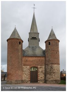 Façade de l’église fortifiée Notre-Dame de La Bouteille en Thiérache, avec deux tours cylindriques en brique encadrant l’entrée, surmontées de toits coniques en ardoise et d’un clocher central élancé sous un ciel nuageux.