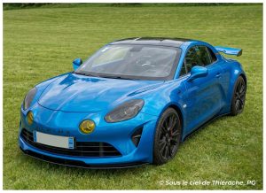 Alpine A110 bleue exposée lors du rassemblement Renault Sport à Saint-Michel en Thiérache, stationnée sur la pelouse du site abbatial avec ses lignes sportives élégantes et ses jantes noires.