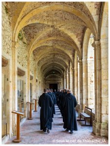 Moines bénédictins déambulant dans le cloître de l’abbaye de Saint-Michel en Thiérache, sous les élégantes voûtes de pierre et de briques, dans une atmosphère paisible et spirituelle empreinte de silence monastique.