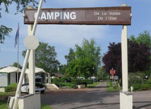 Entrée du camping « De la Vallée de l’Oise » en Thiérache, avec son grand portail en bois, une allée arborée, des emplacements verdoyants et des hébergements de plein air dans un cadre calme et naturel.