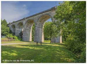 Vue en contre-plongée du viaduc d'Ohis, imposant ouvrage d'art ferroviaire en pierre composé de grandes arches. Entouré d'arbres et d'une prairie verdoyante, il est aujourd'hui un site emblématique de l'Axe Vert de la Thiérache.