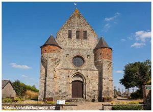 Façade de l'église fortifiée Saint-Rémi de Marly-Gomont, en Thiérache (Aisne), avec ses deux tours défensives en briques et en grès, son portail gothique et son imposante architecture médiévale, sous un ciel bleu d'été.