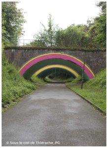Pont ferroviaire voûté situé à Aubenton (Aisne), dont l'arche a été transformée en une œuvre de street art aux couleurs vives. Les bandes rose, verte, jaune et violette dessinent un arc-en-ciel au-dessus de la voie, offrant un contraste original avec la brique de l'ancien pont et la végétation environnante.
